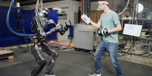 A Photo Showing A Humanoid Robot Wearing Boxing Gloves Facing A Human Wearing Hand Pads.png