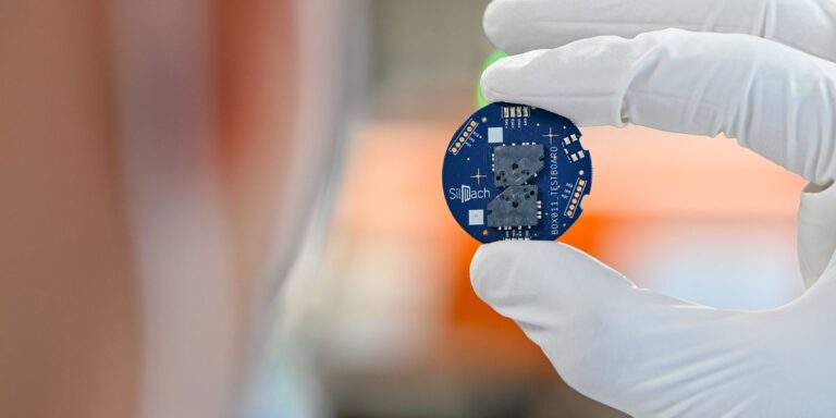 A White Rubber Gloved Hand Holding Up A Small Blue Circle With Computer Chip On It.jpg