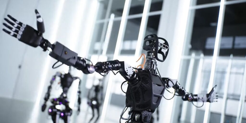 Humanoid Robot Pictured In Foreground With Arms Wide Open Two Other Humanoids Behind It.jpg