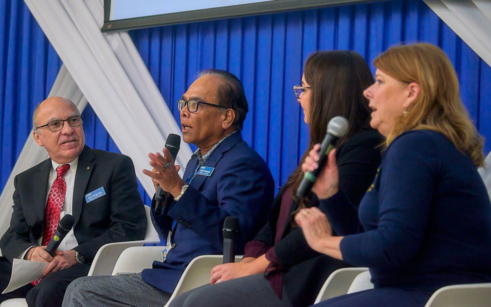 a group of four people sit in chairs and hold speaking microphones while sitting on a stage