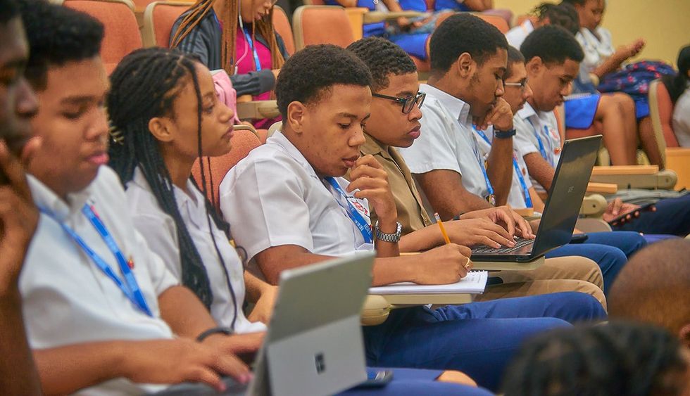 a row of teenagers with laptops and notebooks sit in theater seating