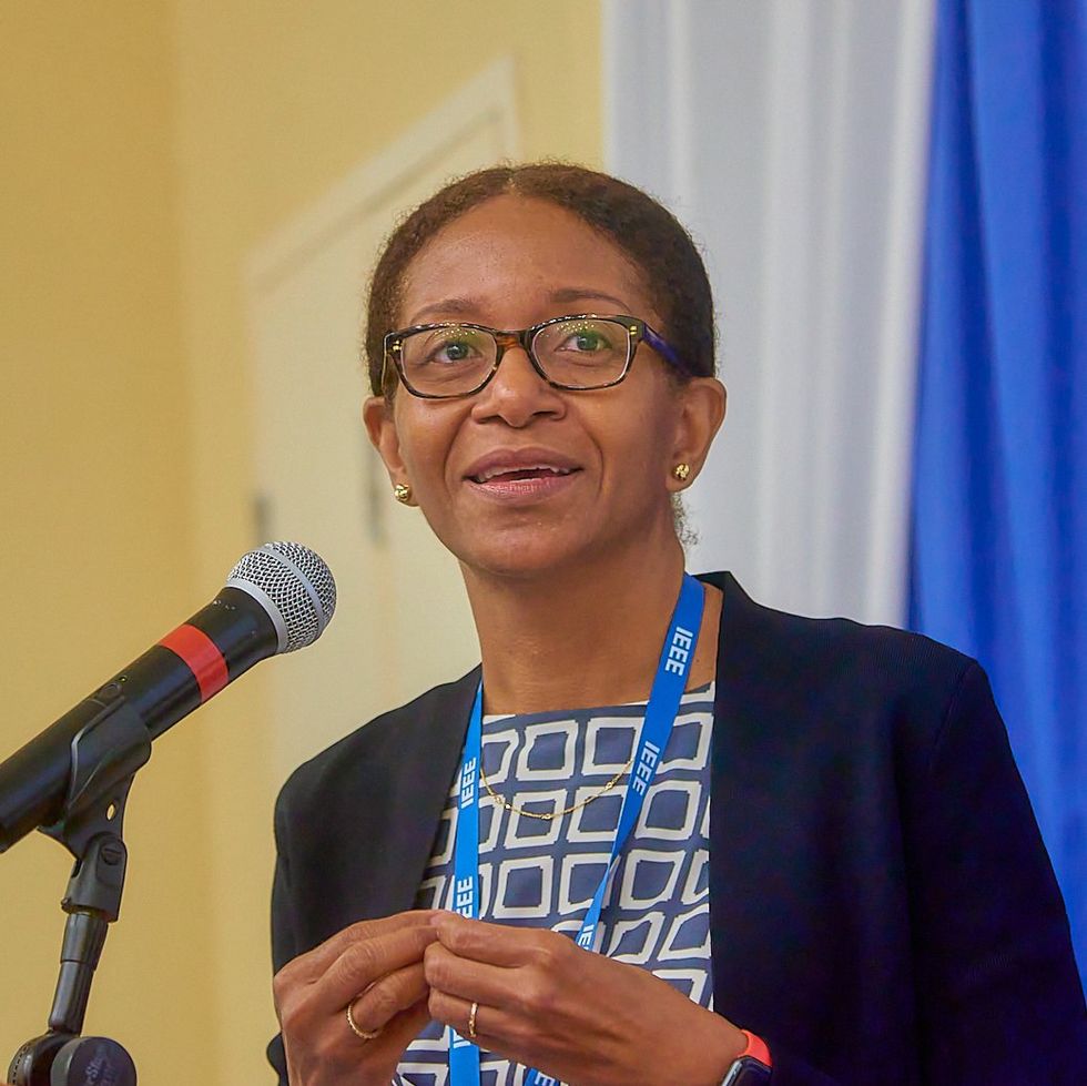 a smiling woman in glasses and an ieee lanyard speaks into a microphone