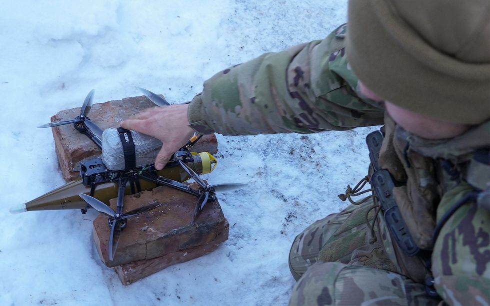 a soldier places his hand on a drone that carries a shell beneath it