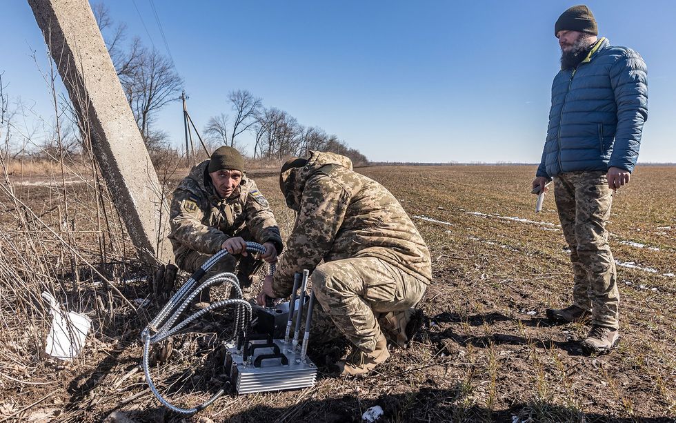 two soldiers work on a piece of machinery consisting of a metal rectangular square with three heavy